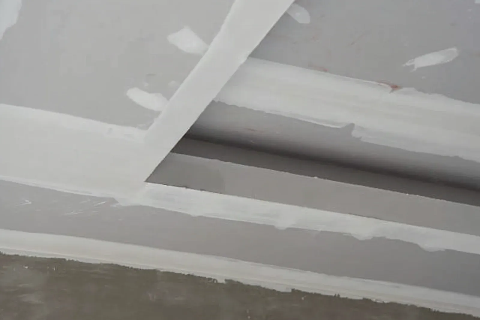 Drywall-wrapped ceiling beams with taped and mudded corners and spotted fasteners, awaiting the next finish coat